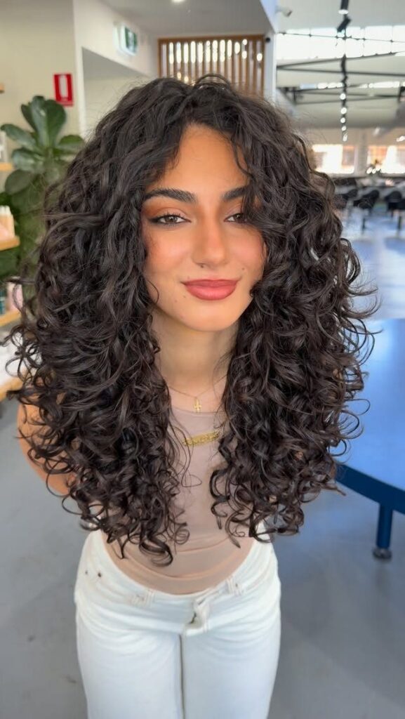 Woman with voluminous dark brown curly hair styled in a layered haircut.