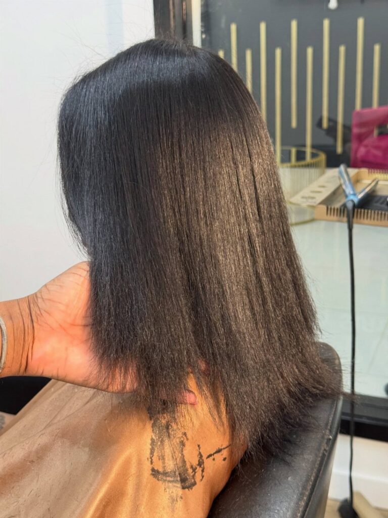 Long straight black hair on a person wearing a brown salon cape.