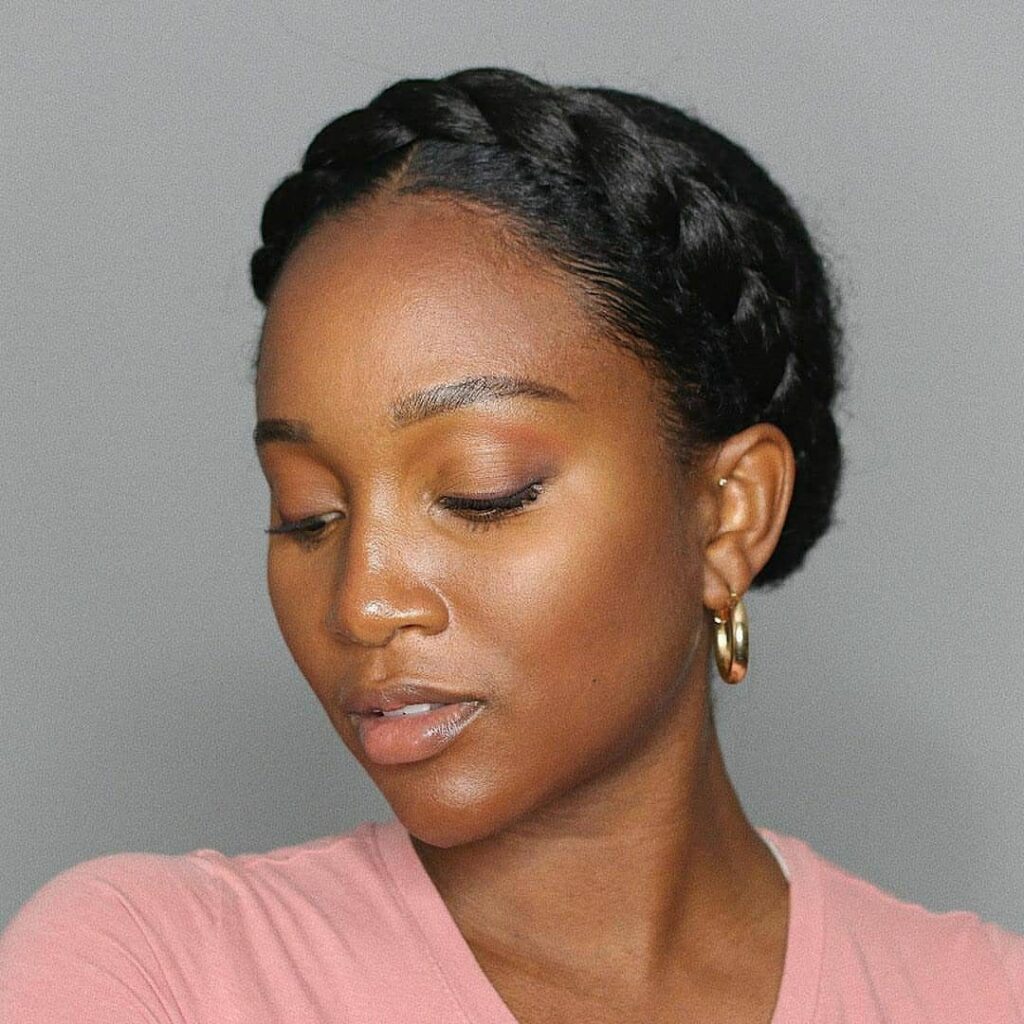 Woman with a braided crown hairstyle, wearing gold hoop earrings and pink shirt.