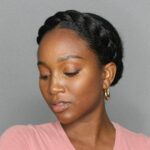 Woman with a braided crown hairstyle, wearing gold hoop earrings and pink shirt.