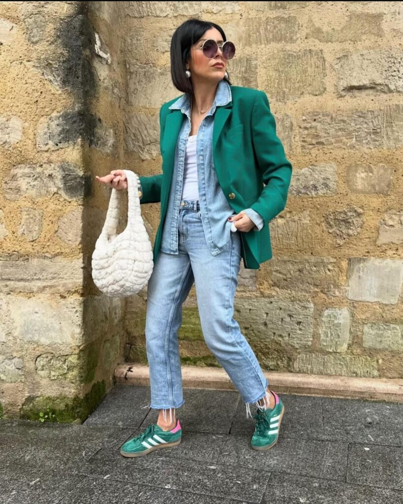 Woman in green blazer and matching green Adidas sneakers standing by stone wall