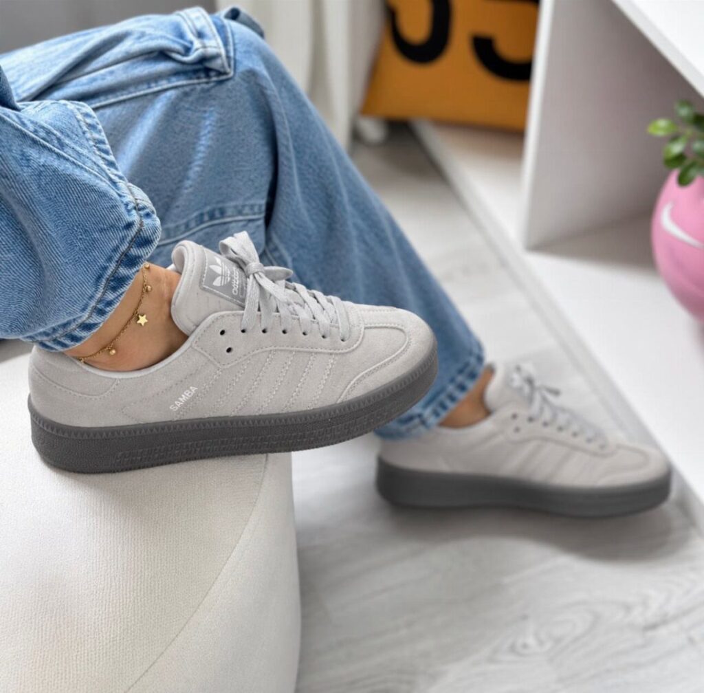 Grey suede Adidas Samba sneakers worn with light blue jeans on a white background