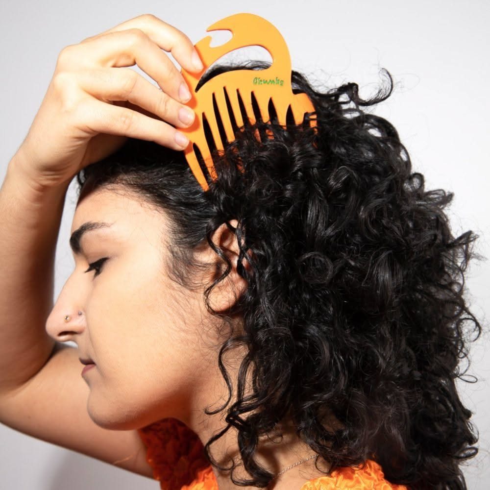Person with curly black hair using an orange afro pick comb in hair