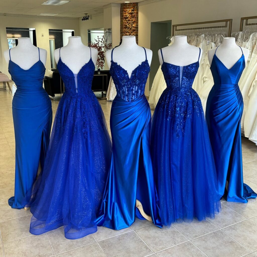 Five royal blue ball dresses and formal gowns displayed on white mannequins.