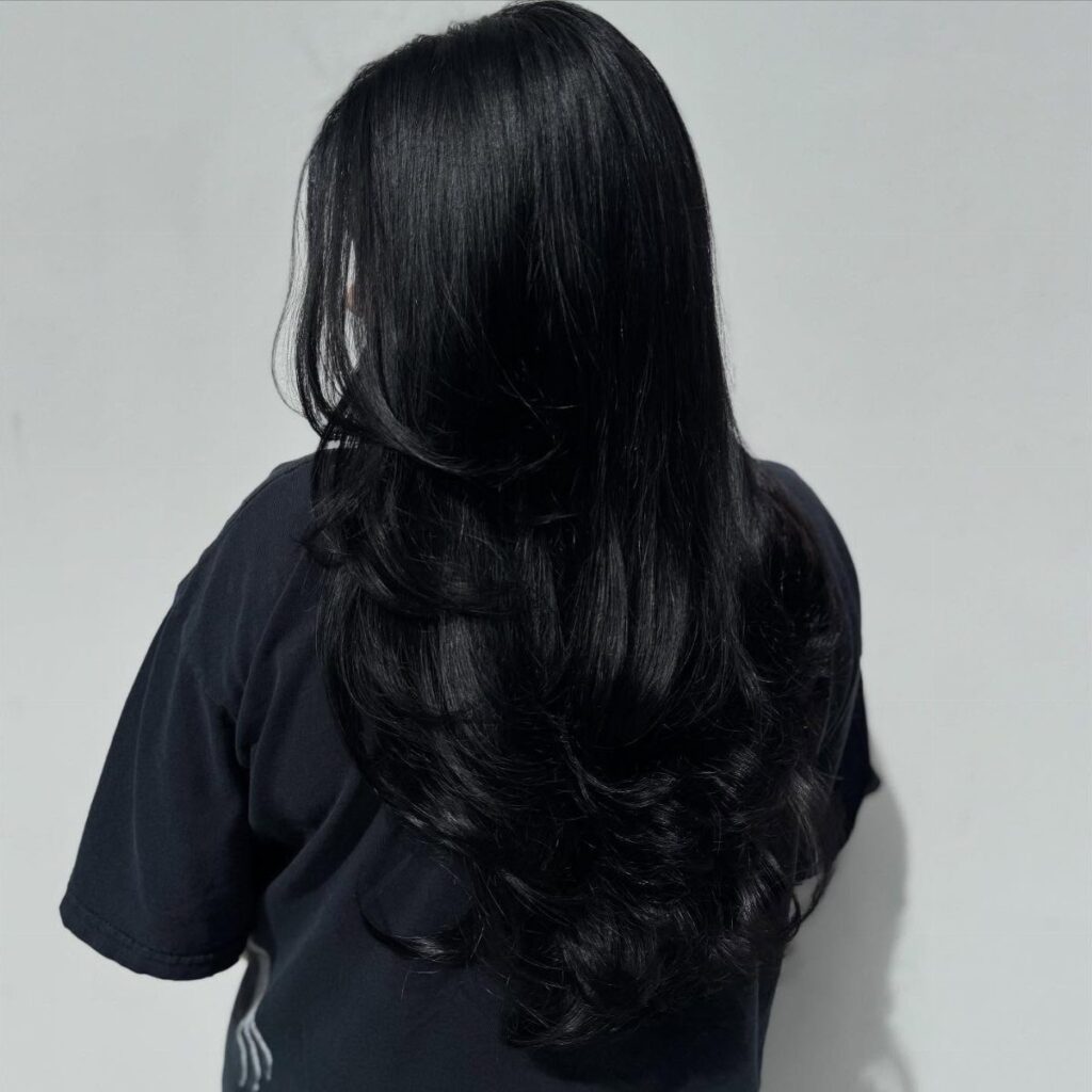 Long wavy black hair seen from behind against a plain gray background