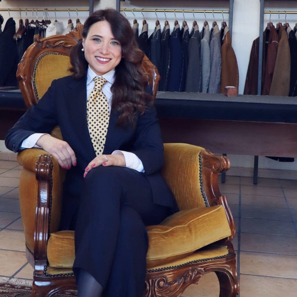 Woman in a navy blue business suit and yellow tie sitting in gold chair