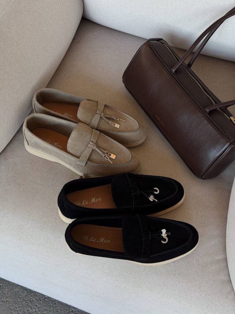 Beige and black loafers next to a brown leather handbag on a grey surface.