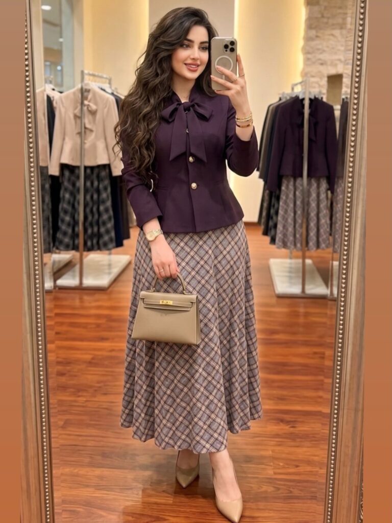 Woman wearing a purple bow blouse and plaid midi skirt in a boutique.