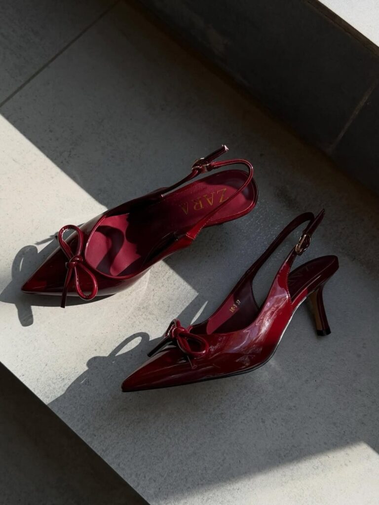 Cherry red kitten heels with bows and slingback straps on a grey stone surface.