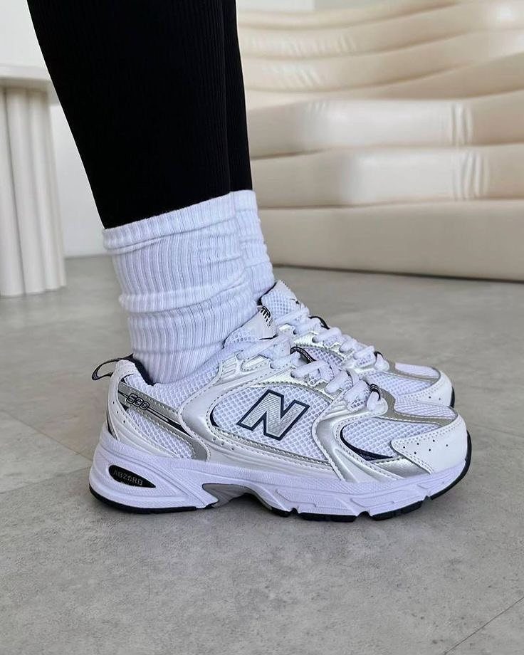 White chunky New Balance sneakers with silver accents and white ribbed socks.