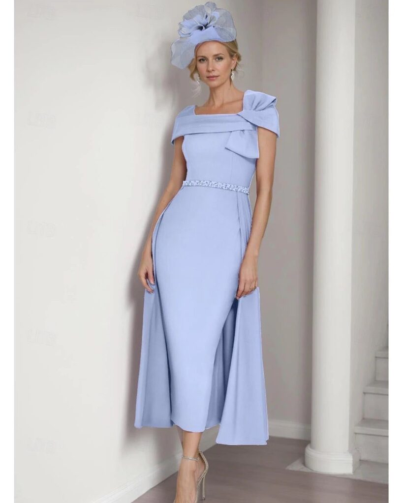 Woman in a light blue formal gown and matching fascinator standing by a column