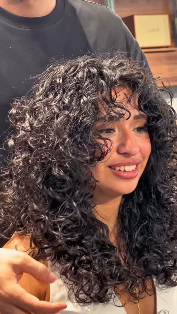 Woman with voluminous dark curly hair smiling while being styled indoors