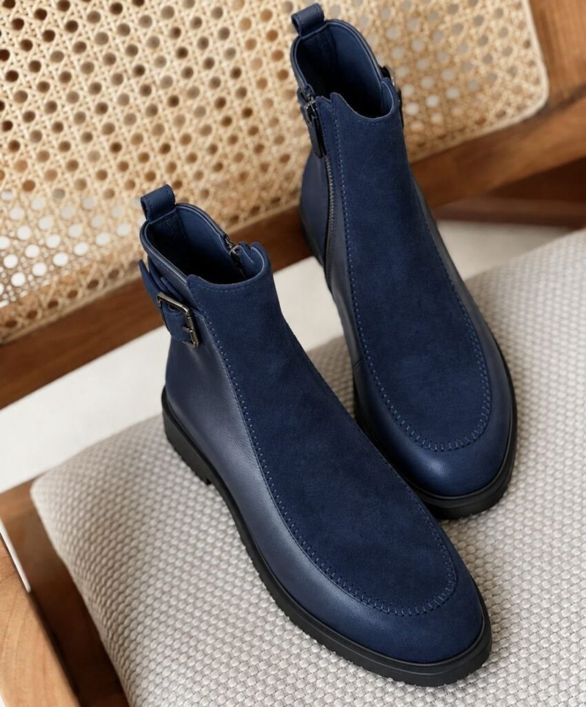 Navy blue nubuck and leather ankle boots resting on a grey fabric chair.