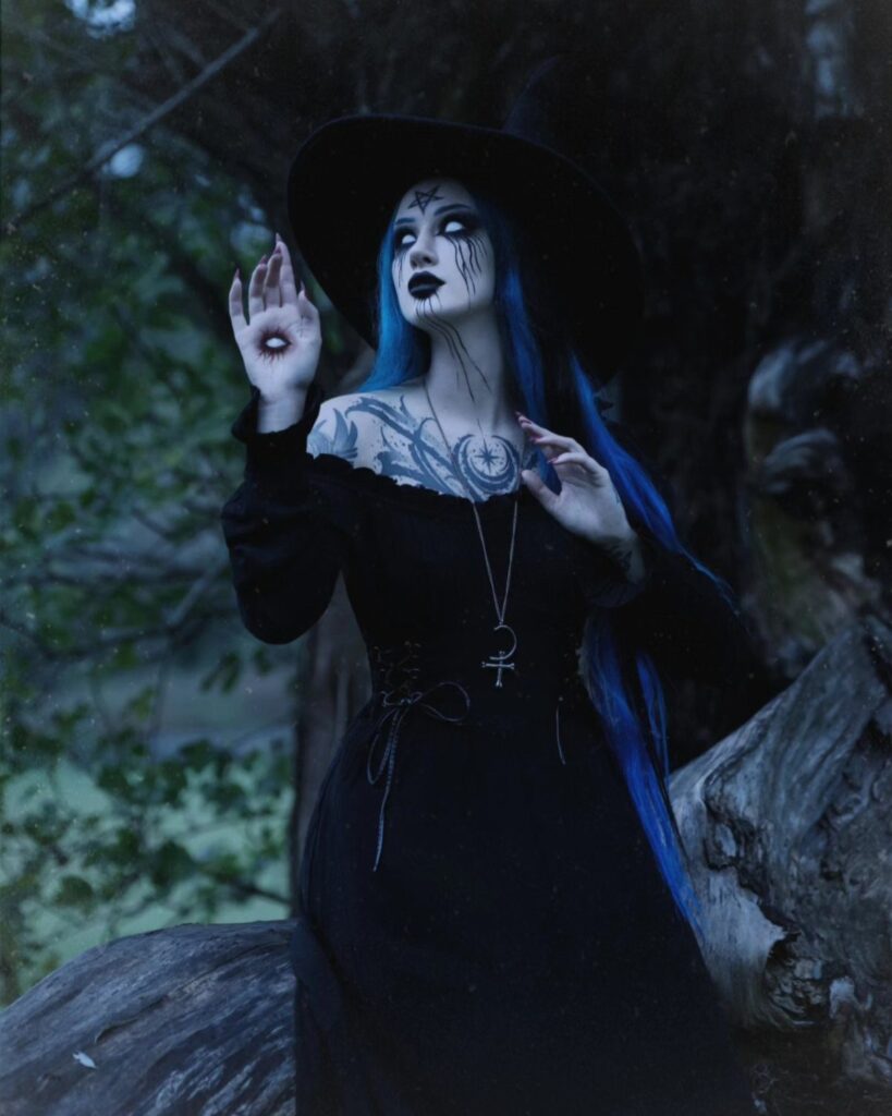 Woman in black witchy clothing and hat posing in a dark forest