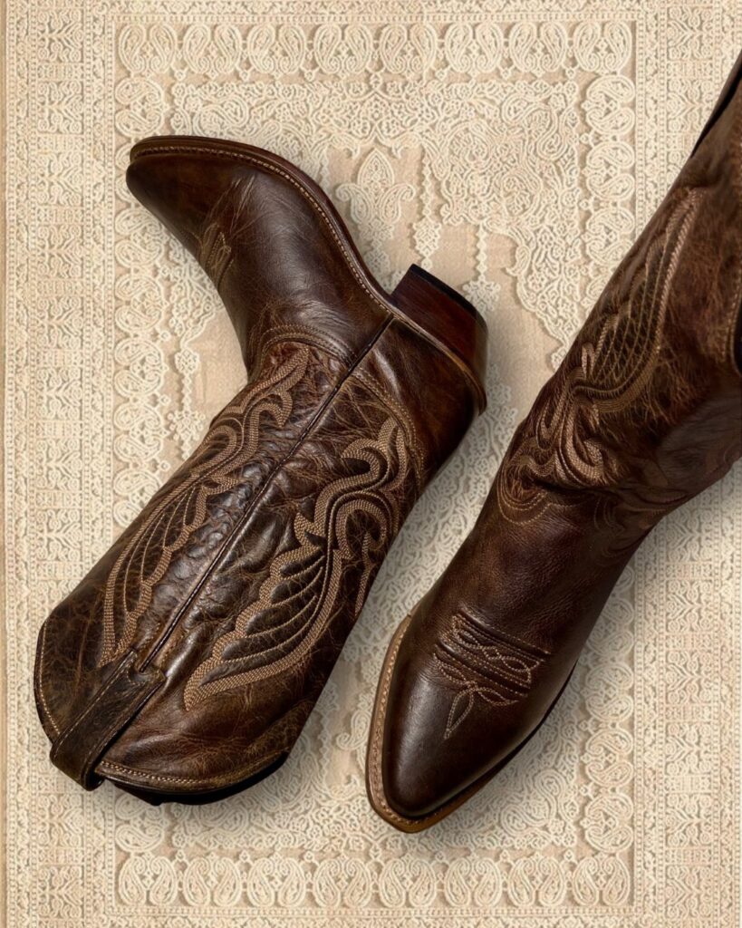 Brown leather cowboy boots with ornate stitching on a cream textured rug