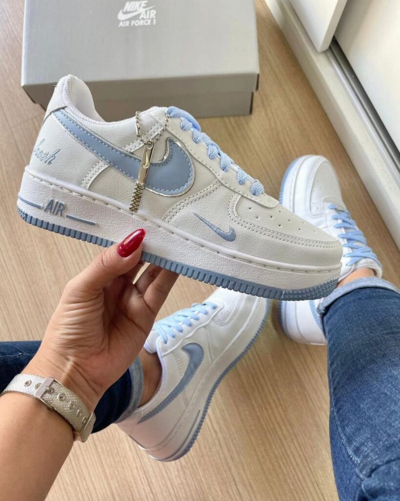 White and light blue Nike sneakers with a gold chain accessory on blue jeans