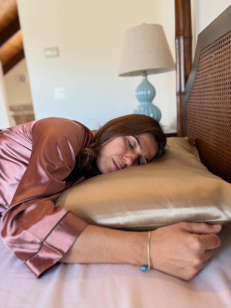 Woman sleeping on a gold silk pillowcase wearing a satin robe in bedroom