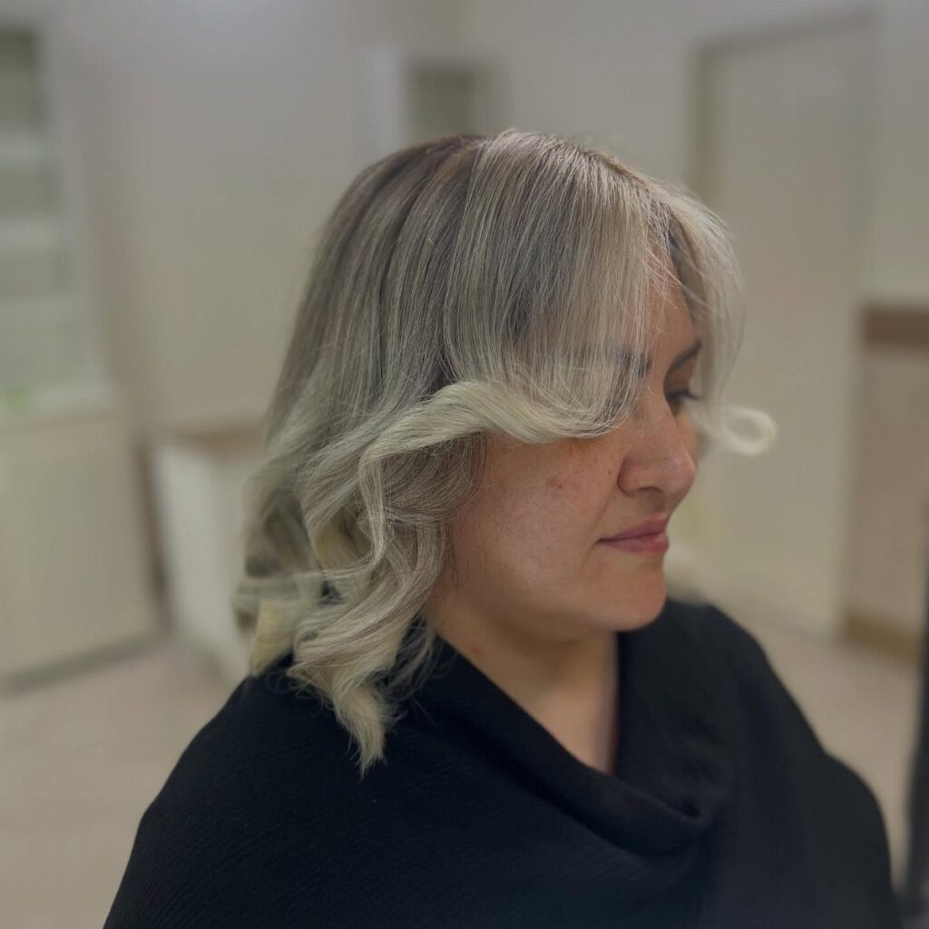 Woman with long blonde hair styled in loose beachy waves and bangs.