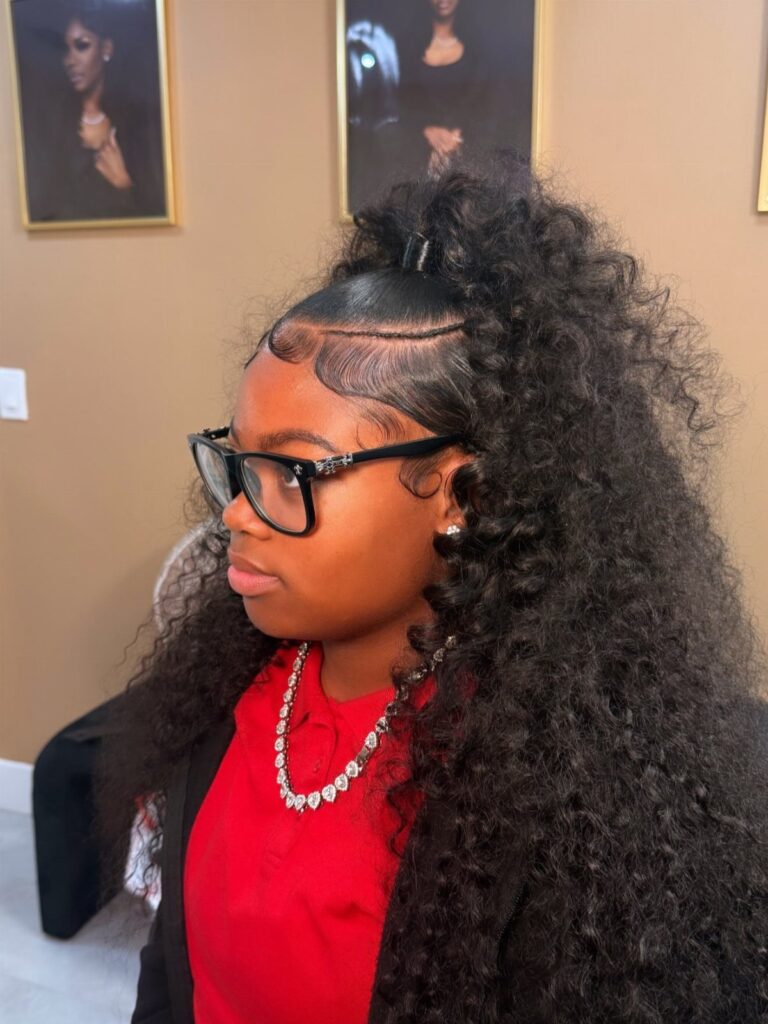 Woman with long voluminous curly hair styled in a half-up ponytail wearing glasses.