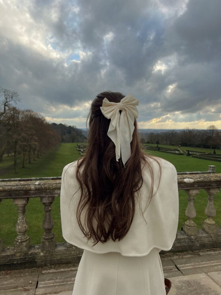Long brown hair styled with a large cream bow overlooking a garden landscape