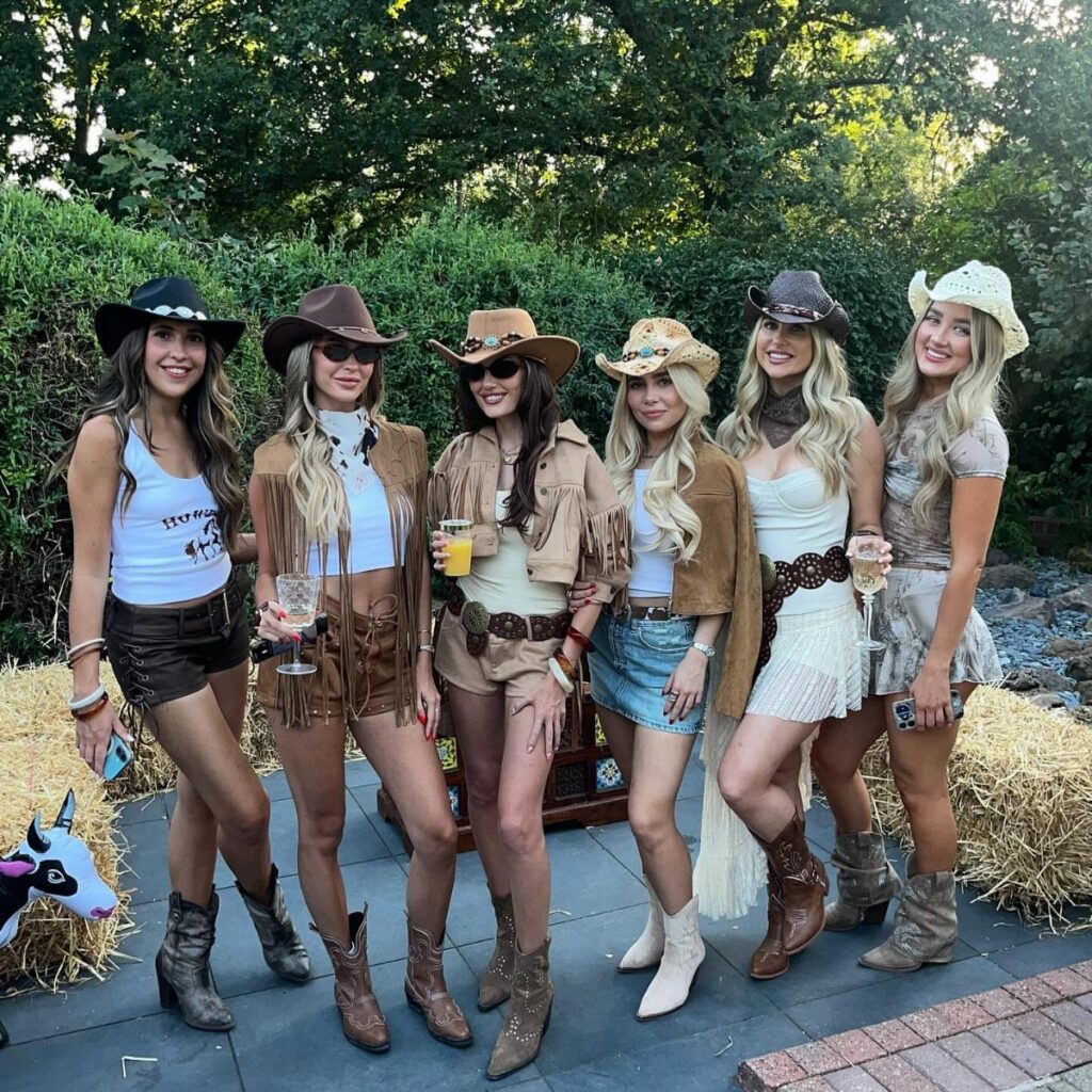 Six women wearing western outfits with cowboy hats and brown leather boots.
