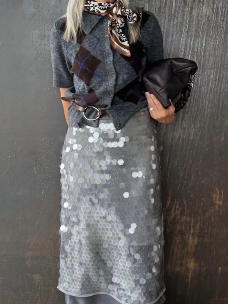 Woman wearing a grey argyle sweater and a shimmering silver sequined midi skirt.