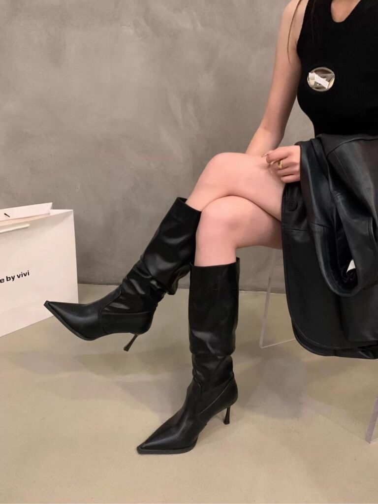 Black leather high heel boots with pointed toes worn by a person sitting.