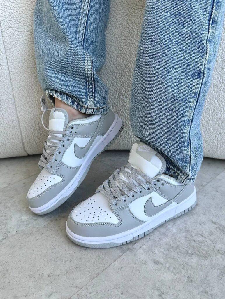 Light grey and white Nike Dunk sneakers worn with light blue denim jeans.