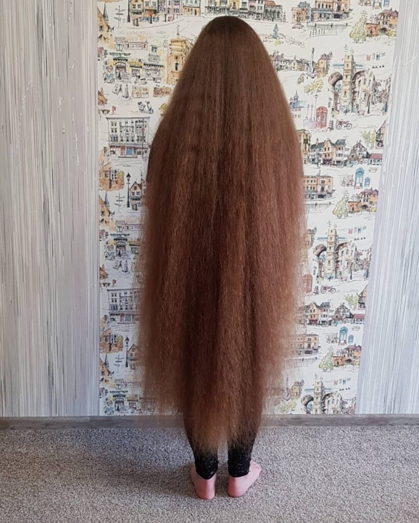 Extremely long reddish-brown hair flowing down to the ankles of a person.