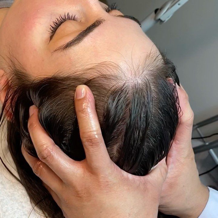 Hands massaging a person's scalp to stimulate hair growth in a salon setting