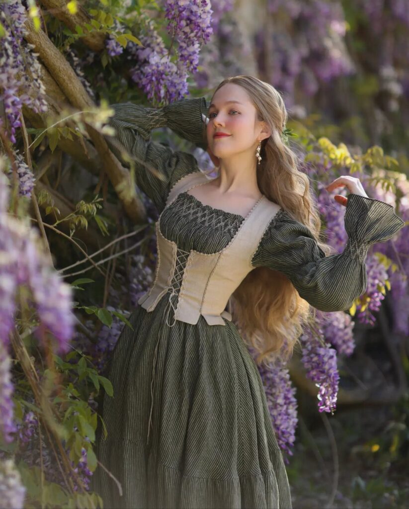 Woman in a medieval dress with a laced bodice among purple wisteria flowers