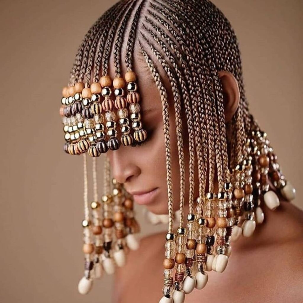 Woman with middle part tribal braids decorated with gold and brown beads.