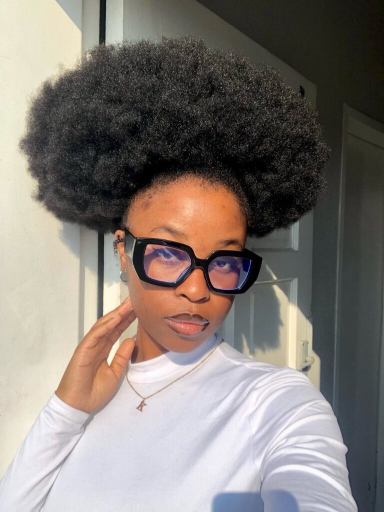 Woman with a large black afro hairstyle wearing black glasses and white shirt.