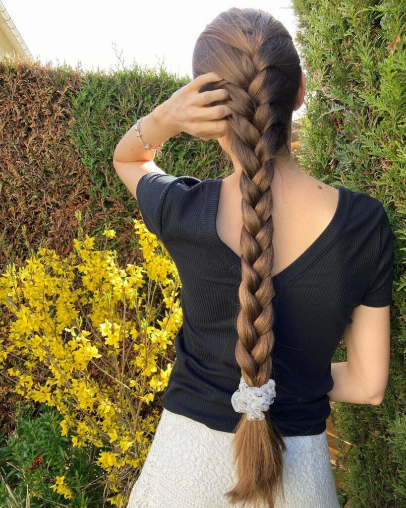 Long brown hair styled in a thick braid from the back outdoors.