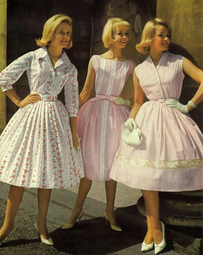 Three women wearing vintage 1960s style floral and pink dresses standing outdoors.