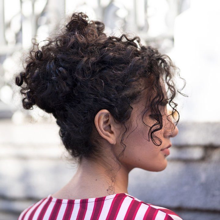 Woman with dark curly hair styled in an elegant updo with loose tendrils.
