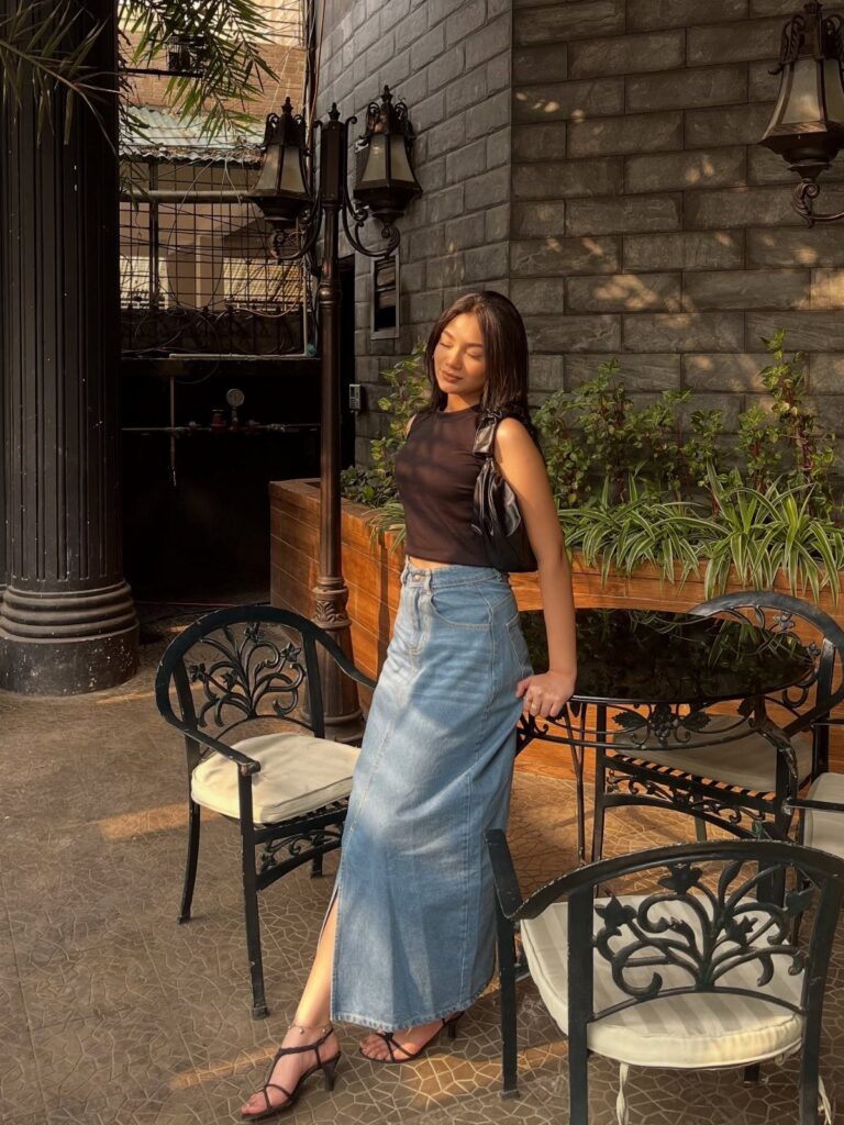 Woman wearing a black sleeveless top and long denim maxi skirt at a cafe