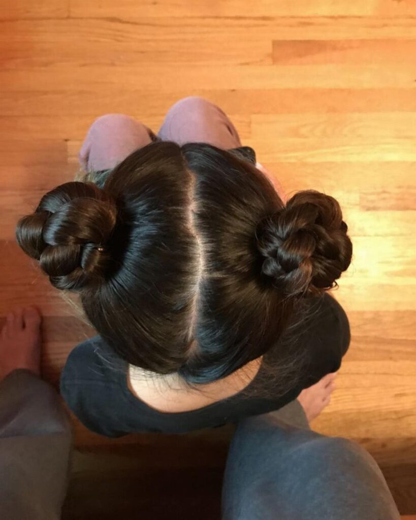 Two braided buns on a person with dark brown hair, viewed from above.