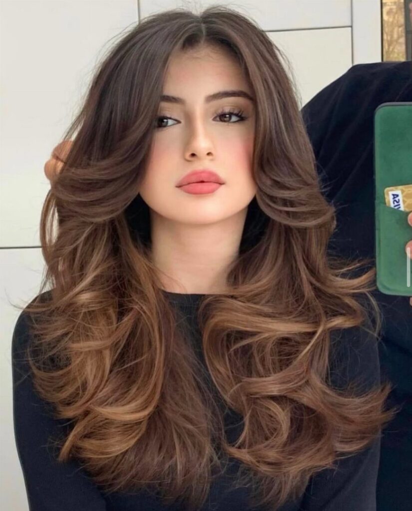 Woman with long brown hair styled in voluminous, bouncy waves and a center part.