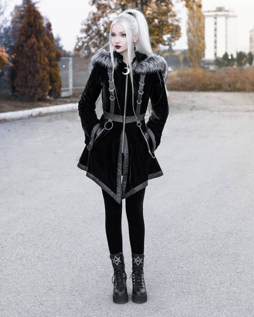Person in black velvet gothic coat with fur collar and platform boots.